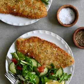 Wiener schnitzel (crispy veal cutlet) on a dinner plate with a side salad and a fork.