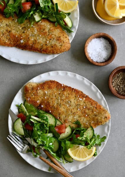 Wiener schnitzel (crispy veal cutlet) on a dinner plate with a side salad and a fork.