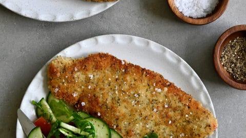 Wiener schnitzel (crispy veal cutlet) on a dinner plate with a side salad and a fork.