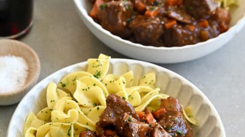 Two bowls containing beef bourguignon and buttered noodles with freshly chopped parsley.