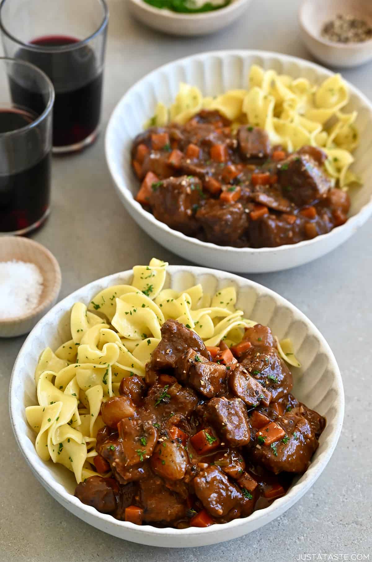 Two bowls containing beef bourguignon and buttered noodles with freshly chopped parsley.