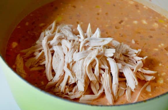 A green stock pot containing chowder and shredded chicken