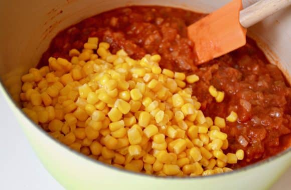 A stock pot containing Salsa Corn Chowder with a pile of yellow corn