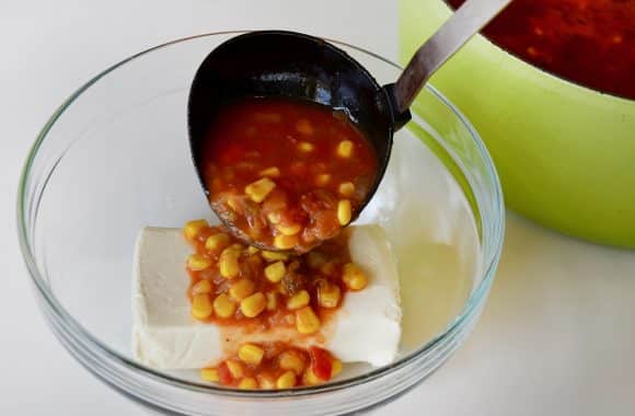 A clear bowl containing cream cheese with chowder being ladled in