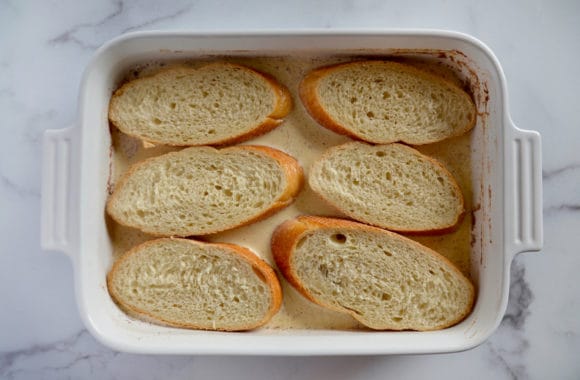 Sliced baguette soaking in eggnog custard