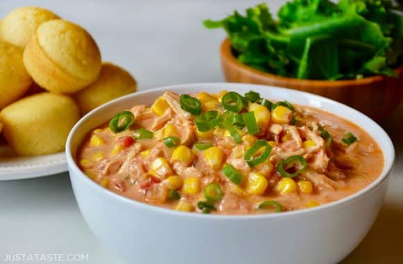 A white bowl containing Salsa Corn Chowder with a salad and corn muffins in the background