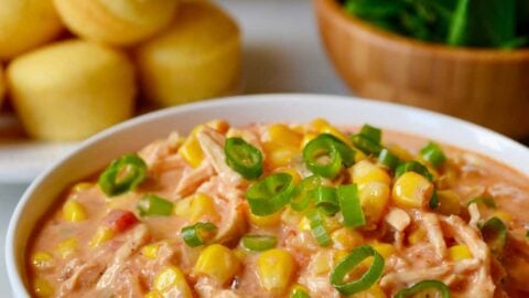 A white bowl containing Salsa Corn Chowder with a plate of corn muffins behind it