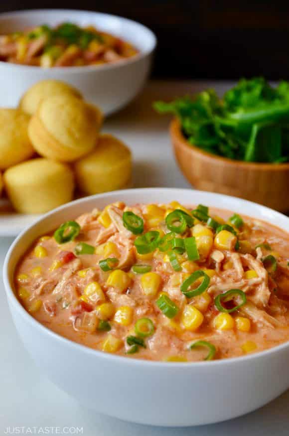 A white bowl containing Salsa Corn Chowder with a plate of corn muffins behind it