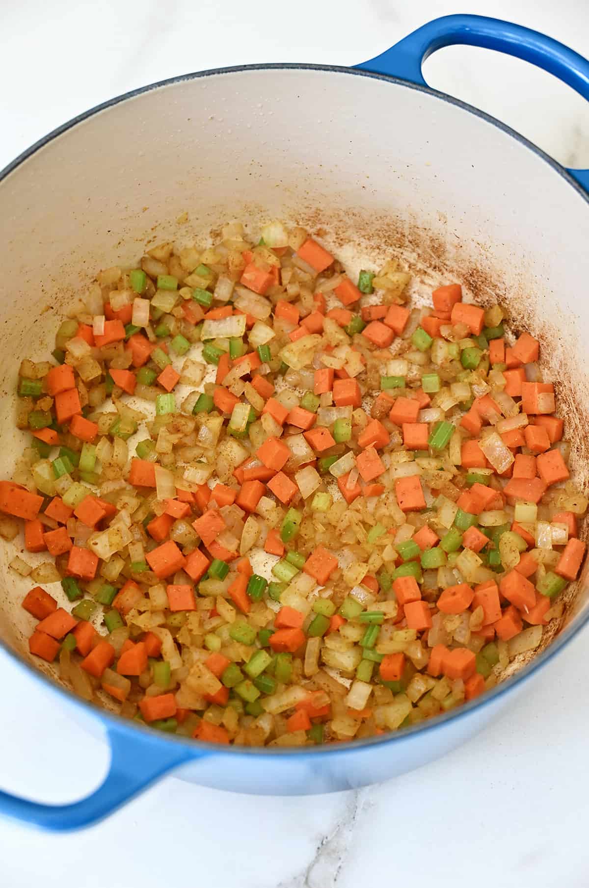 A dutch oven containing sautéed carrots, celery and pearl onions.