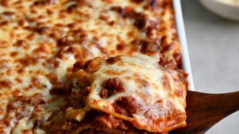 A wooden spatula lifts a slice of lasagna out of a baking dish.