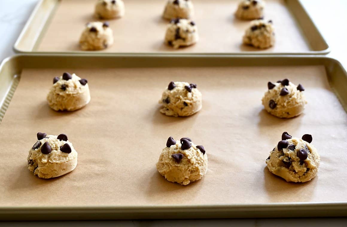 Scoops of chocolate chip cookie dough on parchment paper-lined baking sheets