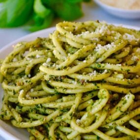 Basil pesto pasta on a white plate with basil and cheese