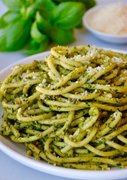 Basil pesto pasta on a white plate with basil and cheese