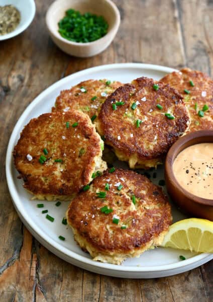 Maryland-style crab cakes on a plate with a small bowl containing remoulade for dipping.