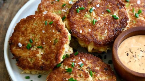 Maryland-style crab cakes on a plate with a small bowl containing remoulade for dipping.