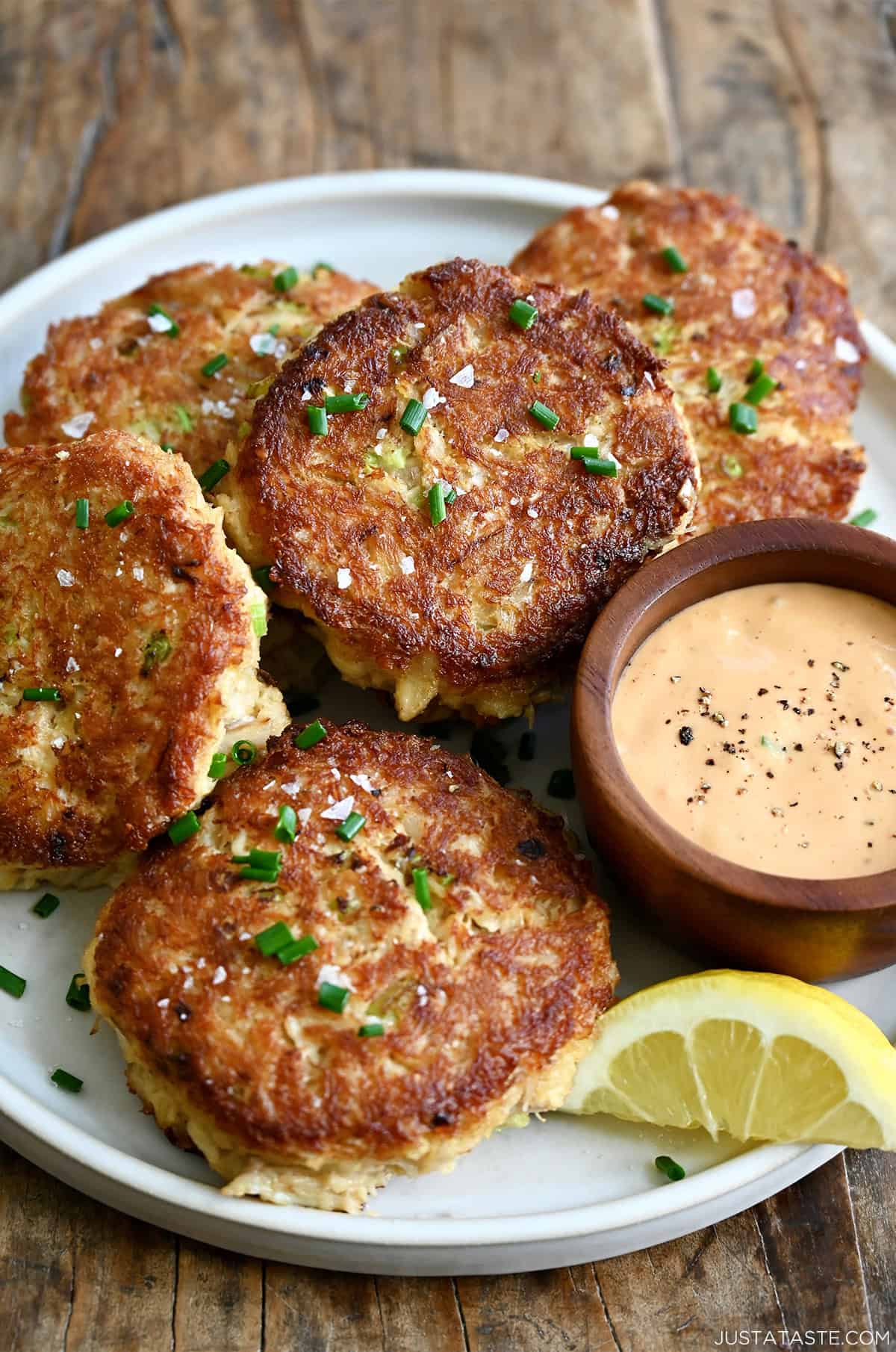 Easy Maryland crab cakes with a crispy, golden crust on a plate with lemon slices and a bowl containing remoulade.