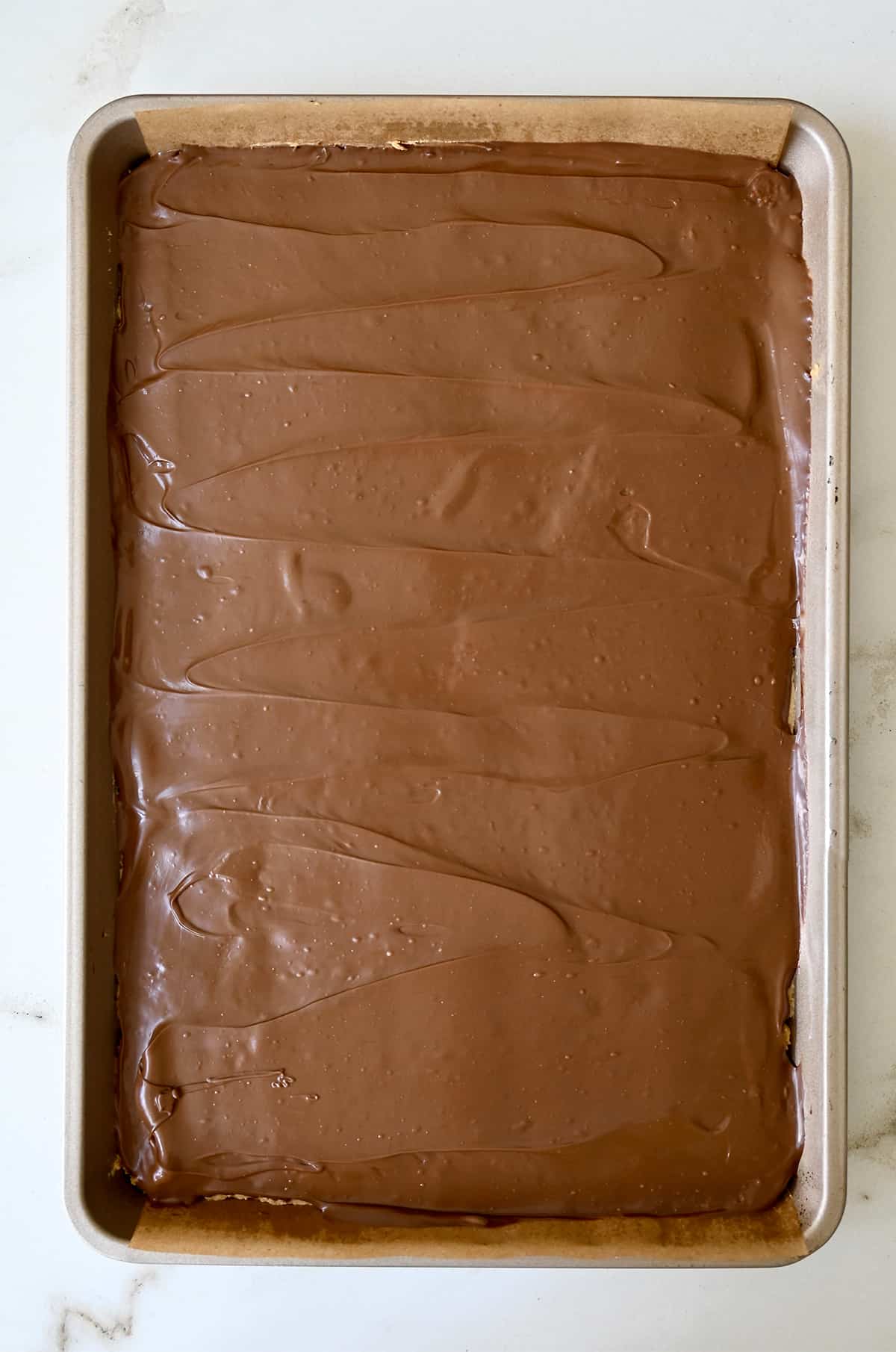 Melted chocolate atop peanut butter bars on a baking sheet.