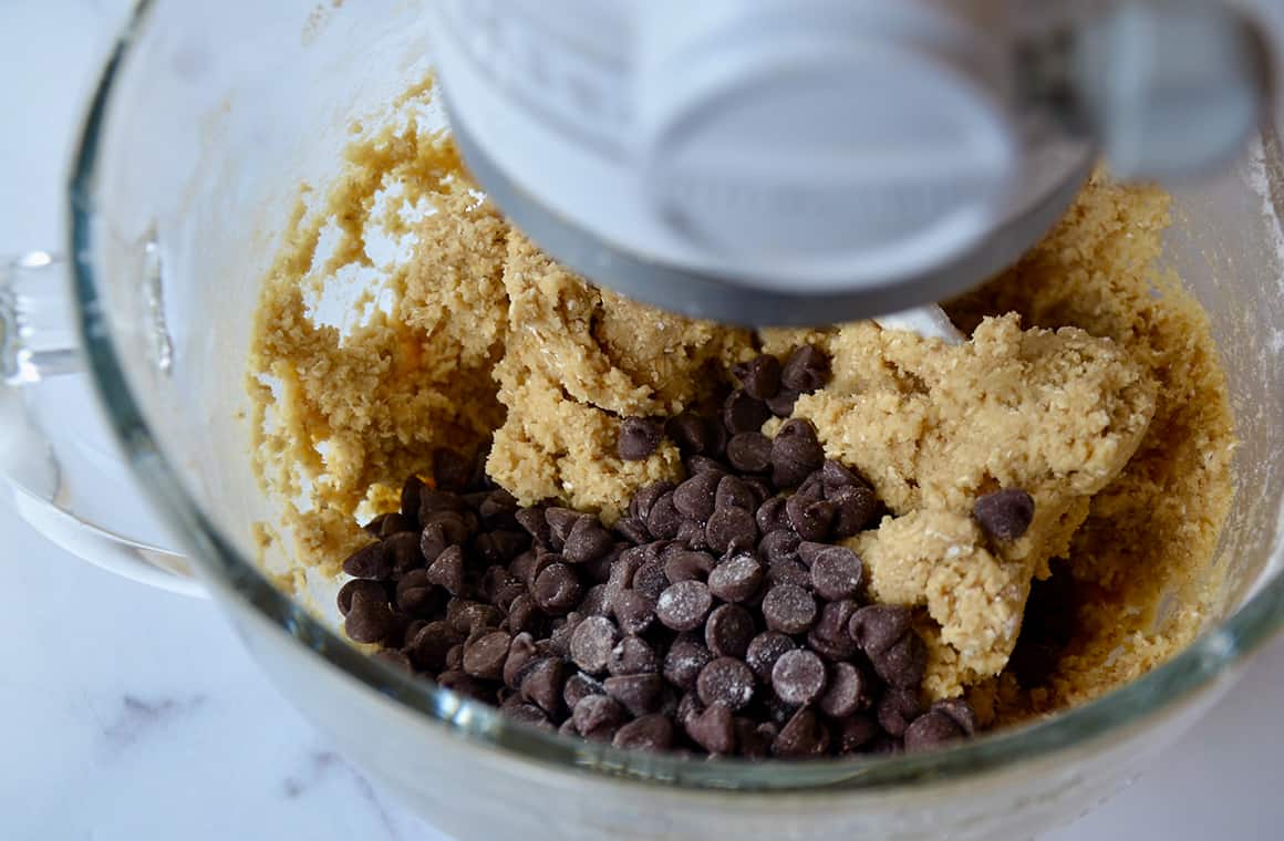 Bowl of stand mixer containing cookie batter and chocolate chips
