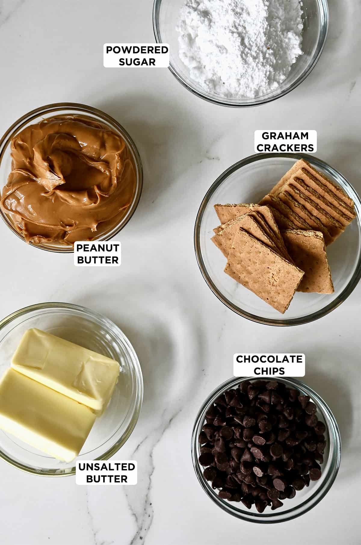 Glass bowls containing creamy peanut butter, powdered sugar, graham crackers, chocolate chips and two sticks of butter.