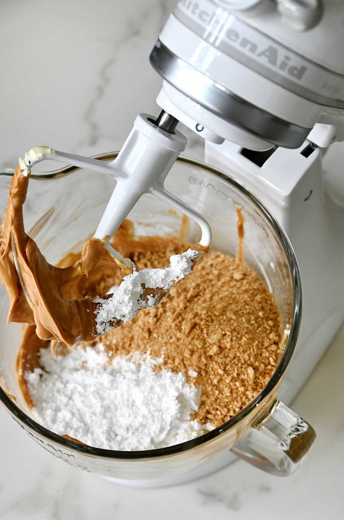 A stand mixer bowl containing creamy peanut butter, graham cracker crumbs and powdered sugar.