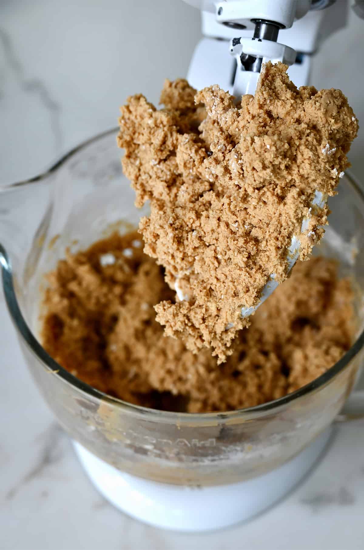 A peanut butter and graham cracker crumb mixture covering the paddle attachment of a stand mixer.