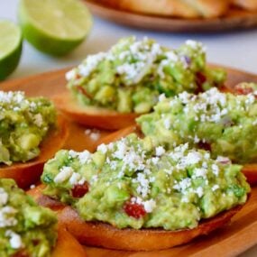 Guacamole bruschetta toasts on a wooden plate