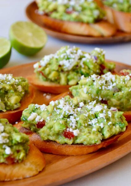 Guacamole bruschetta toasts on a wooden plate
