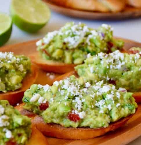 Guacamole bruschetta toasts on a wooden plate