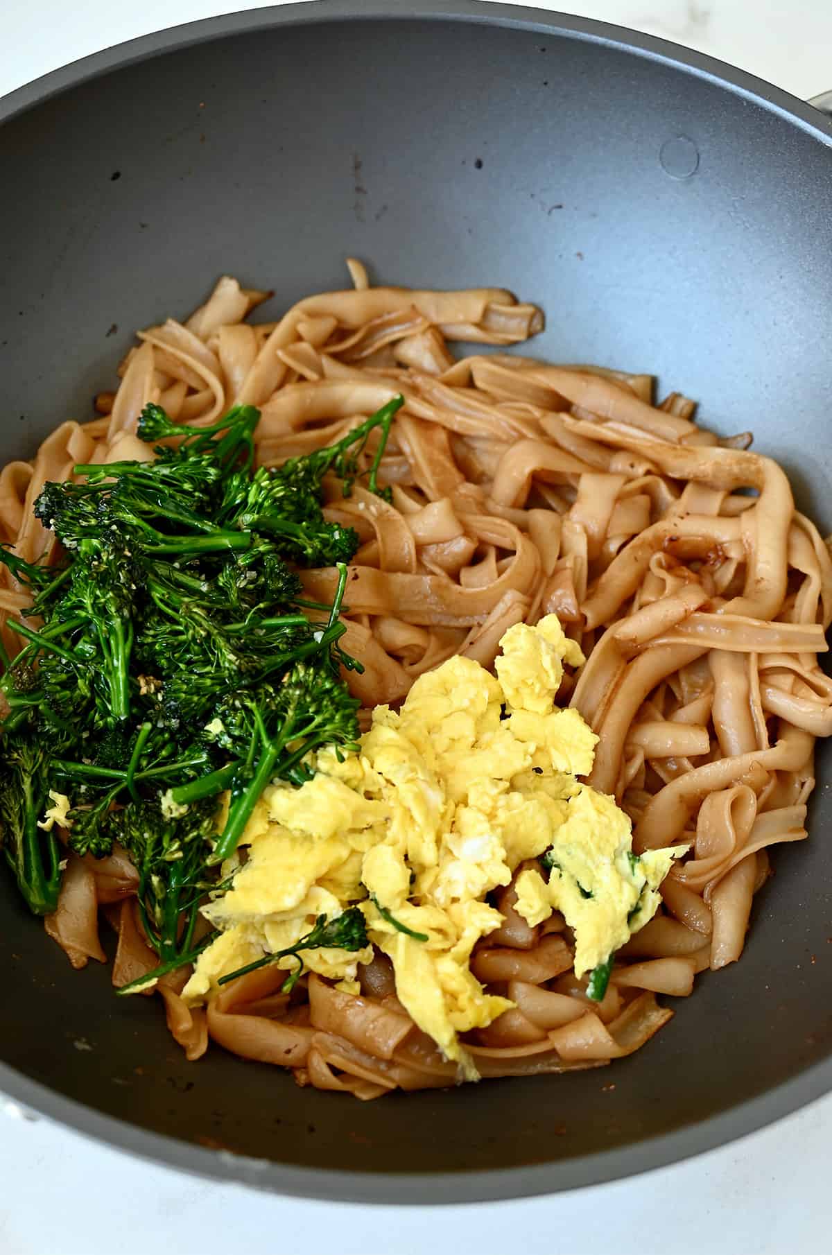 Broccolini, scrambled eggs and caramelized rice noodles in a wok.