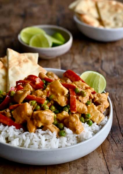 Coconut curry chicken with peas and bell peppers served with basmati rice, naan, and a lime wedge.