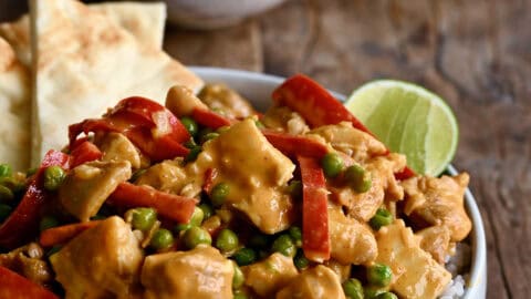 Coconut curry chicken with peas and bell peppers served with basmati rice, naan, and a lime wedge.