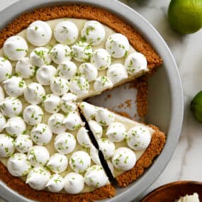 A top-down view of The Best Key Lime Pie in a pie plate topped with dollops of whipped cream