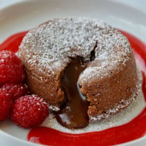 Chocolate Lava Cake on white plate with raspberry sauce and fresh raspberries