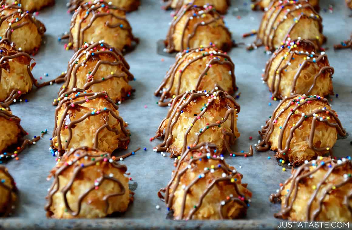 Coconut macaroons on a baking sheet drizzled with milk chocolate and topped with sprinkles