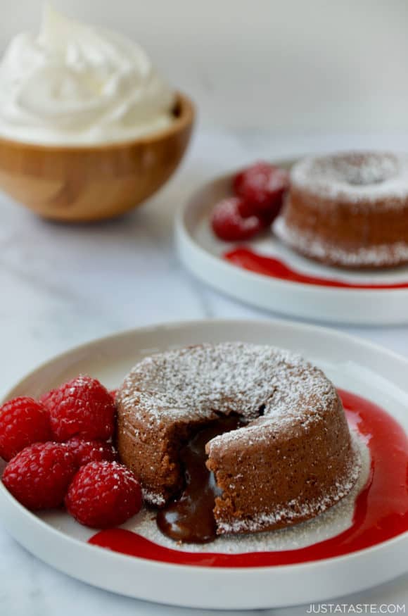 Chocolate Lava Cakes with Raspberry Sauce on dessert plates with fresh raspberries; bowl with whipped cream