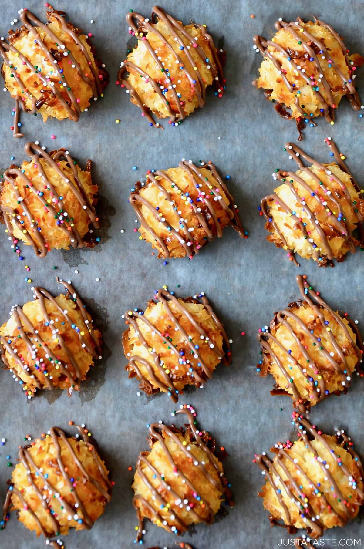 Golden coconut macaroons with glossy chocolate drizzle cooling on parchment paper.