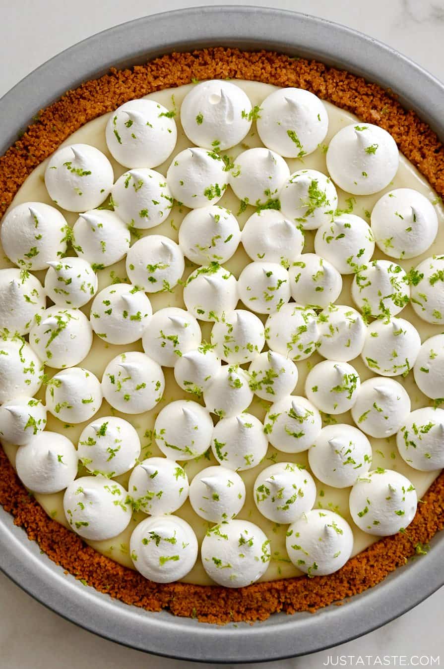 A top-down view of key lime pie topped with dollops of whipped cream and grated lime zest
