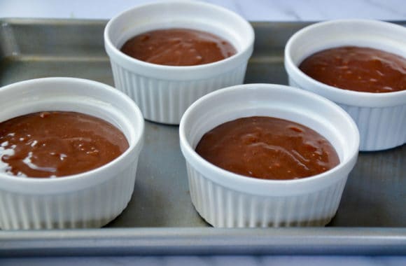 Four ramekins containing lava cake batter on baking sheet 