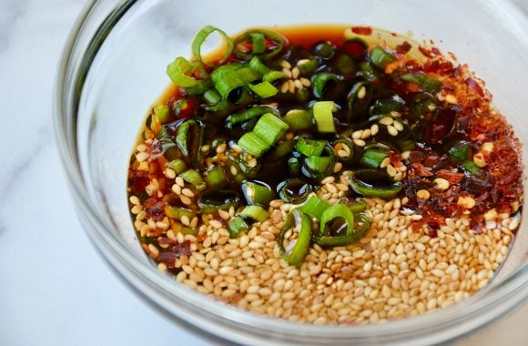 Small clear bowl containing spicy garlic sauce with scallions and sesame seeds