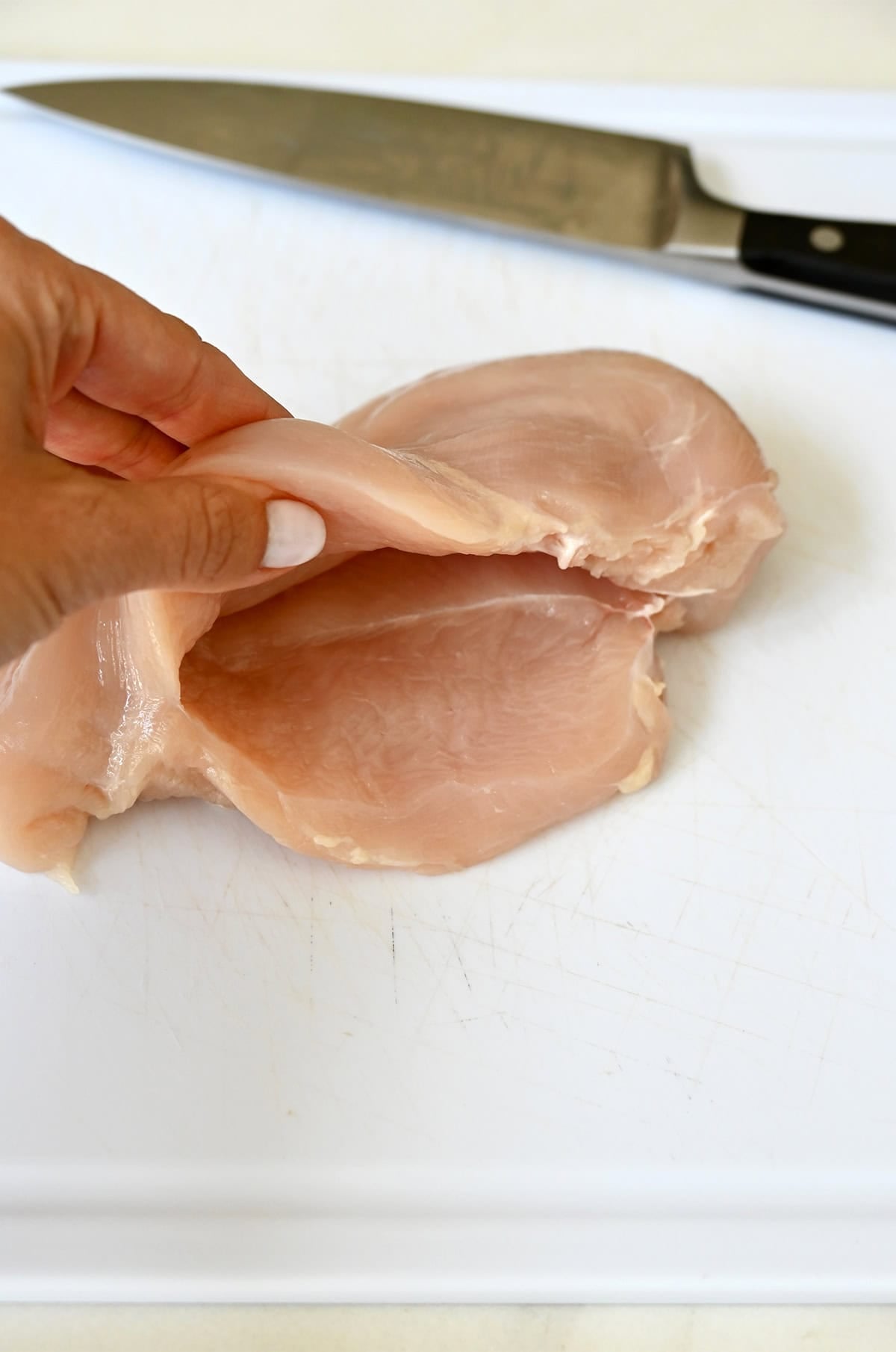 A raw chicken breast on a cutting board with a deep horizontal pocket cut into the side, ready to be stuffed.