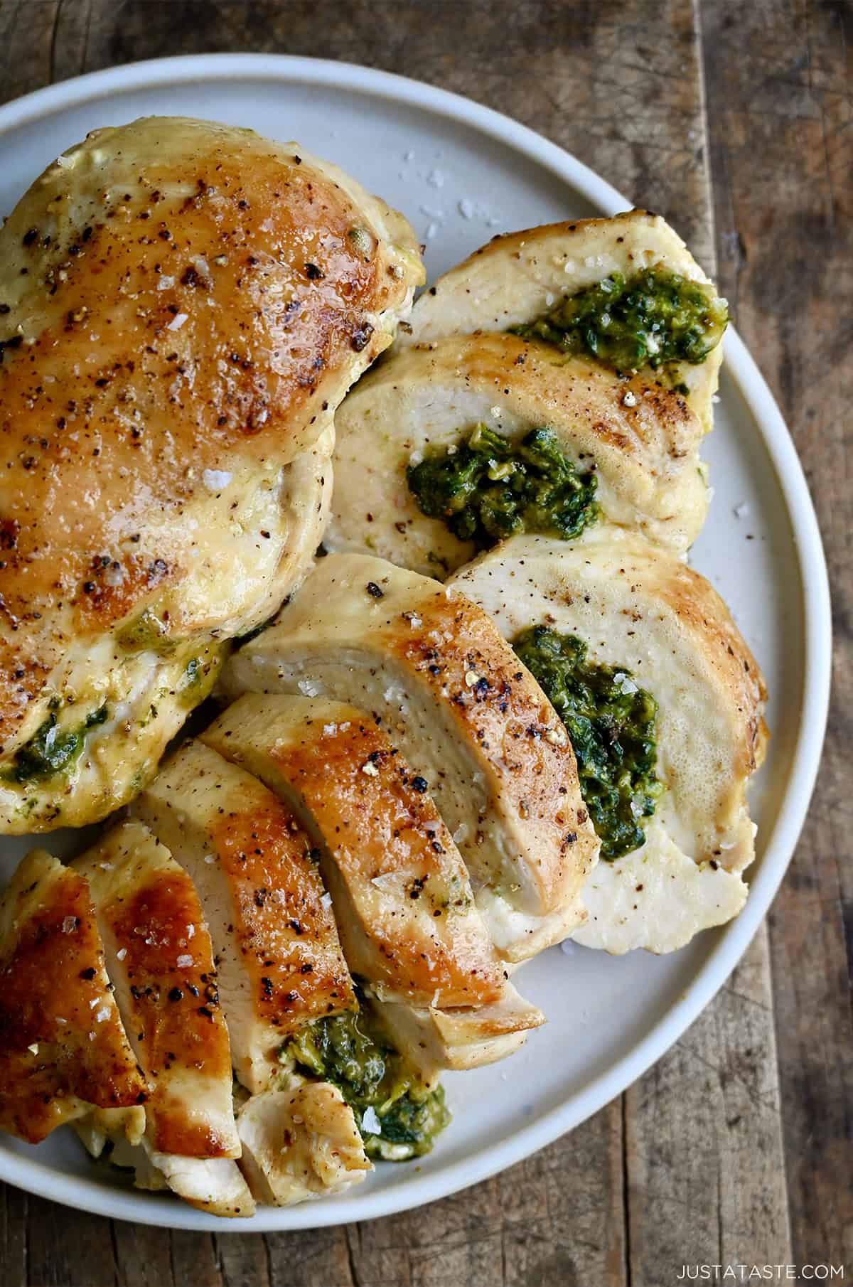 A close-up of two spinach stuffed chicken breasts on a white plate, golden brown on the outside with the cheesy filling visible at the edges.