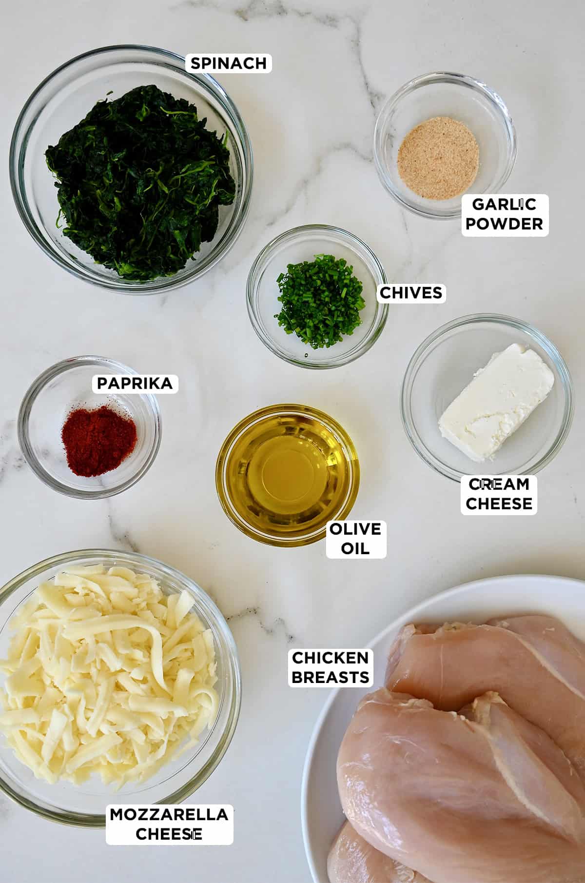 The ingredients for spinach and mozzarella stuffed chicken breasts including frozen spinach, shredded mozzarella, cream cheese, fresh chives, garlic powder, smoked paprika, boneless skinless chicken breasts and olive oil.