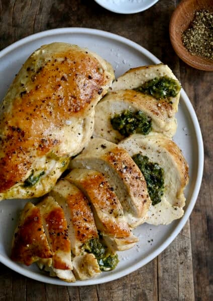Two spinach and cheese stuffed chicken breasts on a dinner plate with one cut into slices to expose the cheesy filling.