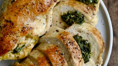Two spinach and cheese stuffed chicken breasts on a dinner plate with one cut into slices to expose the cheesy filling.