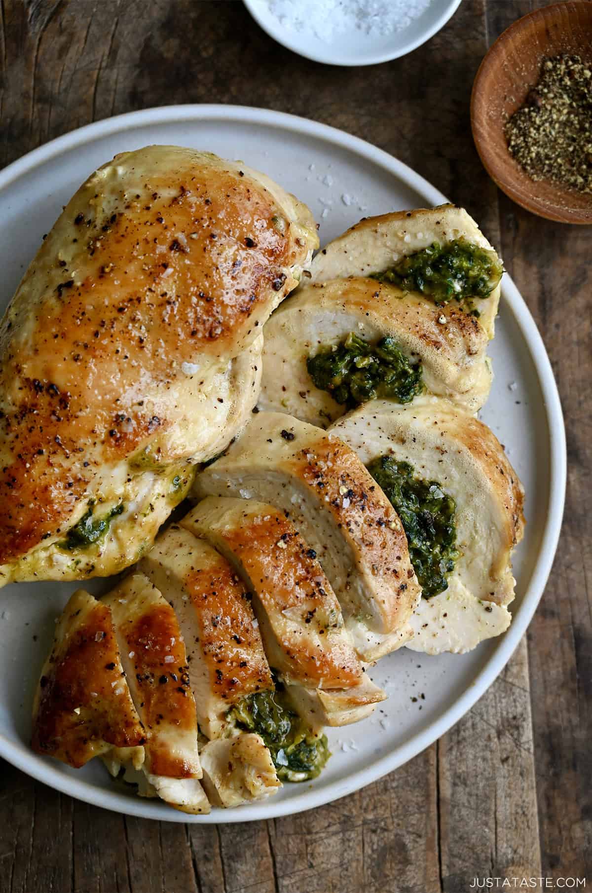 Two spinach and cheese stuffed chicken breasts on a dinner plate with one cut into slices to expose the cheesy filling.