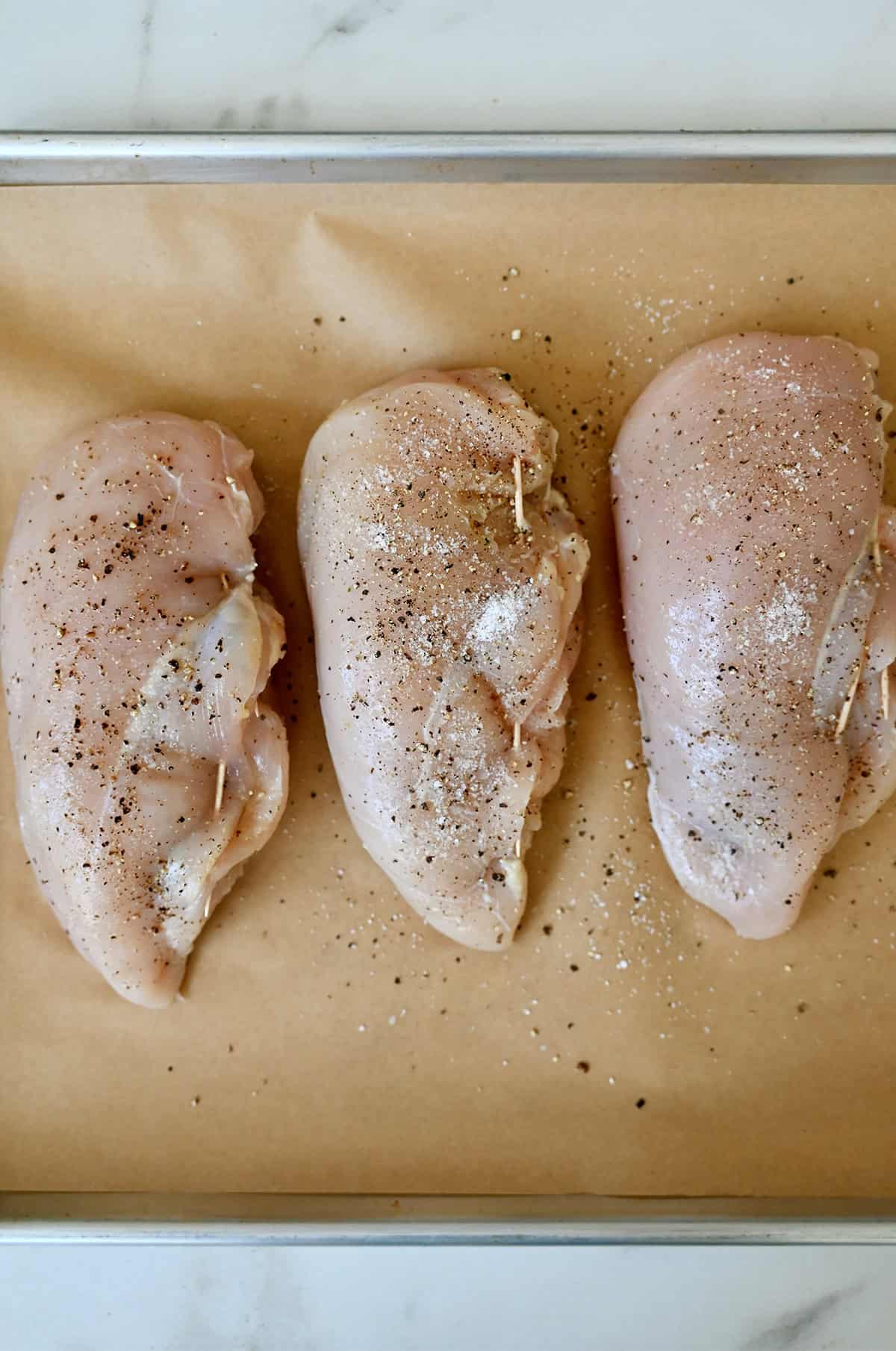 Raw stuffed chicken breasts with toothpicks on a parchment paper-lined baking sheet.