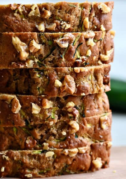 Slices of healthy zucchini bread with walnuts stacked six high on a cutting board.