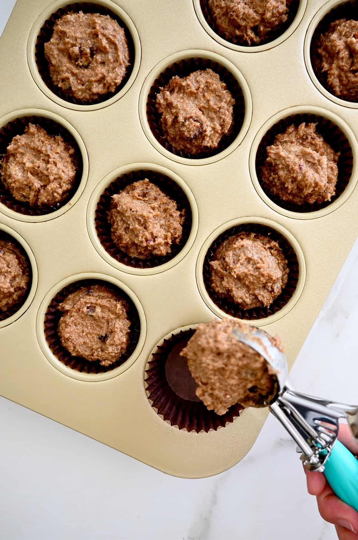 Scooping bran muffin batter into a lined muffin tin.