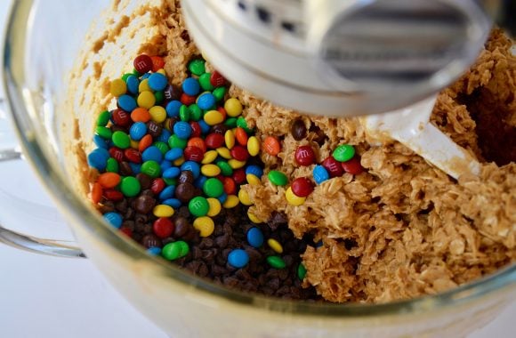 Stand mixer bowl with monster cookies batter, mini chocolate chips and M&Ms