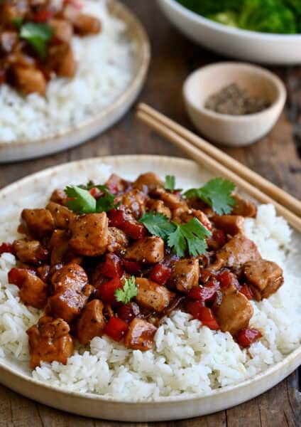 Black pepper chicken over white rice on a plate with chopsticks.
